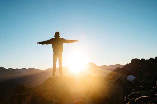 Figure standing on mountain top with sun setting in background